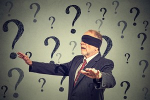 Portrait business man blindfolded stretching his arms out walking through many questions isolated on gray wall background